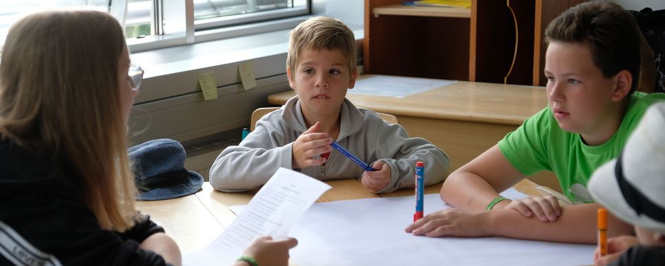 Kinder sitzen mit Stiften um Flipchart. Foto: Hanner