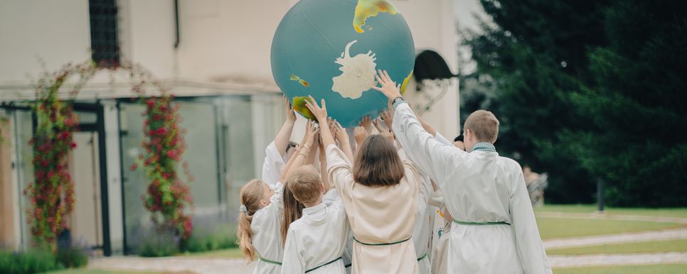 Eine Gruppe Ministrant*innen hält gemeinsam eine große aufblasbare Weltkugel über ihren Köpfen.