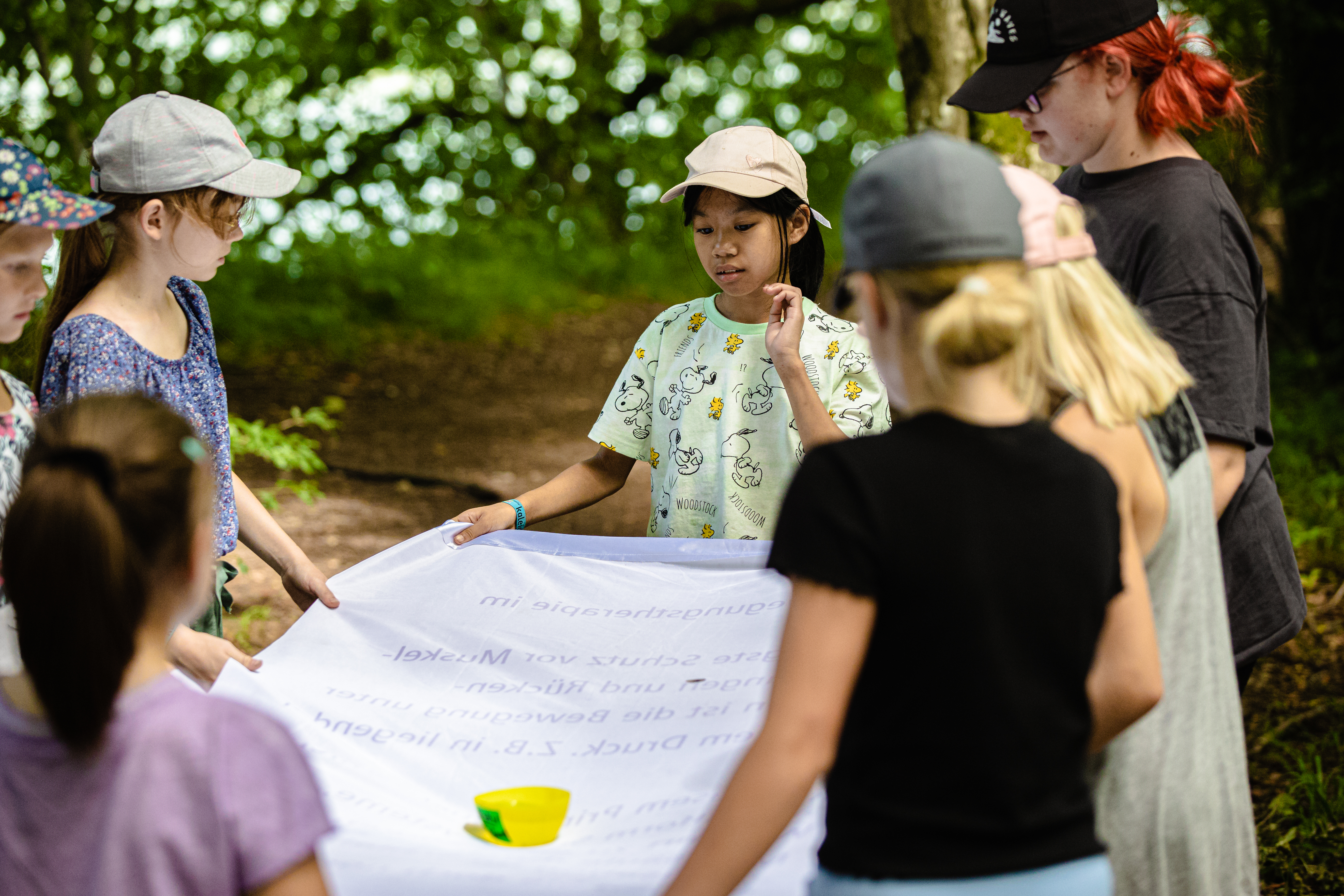 Mehrere Kinder stehen im Kreis um einen Tisch. Hinter ihnen ist der Wald zu sehen.